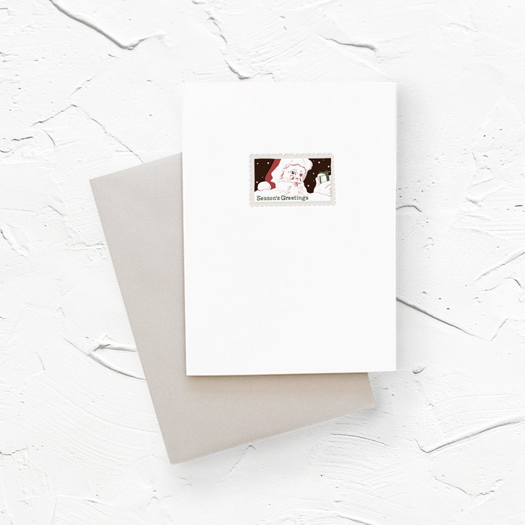 White card with postage stamp image in center with image of Santa Claus and black text saying,