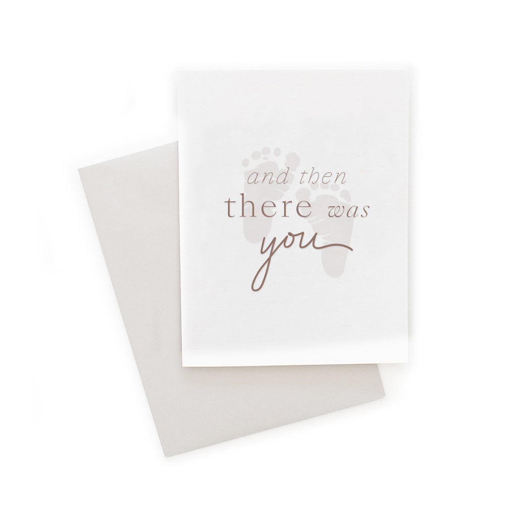 White card with image of baby’s footprints and gray text saying, “And Then There Was You”. A gray envelope is included.