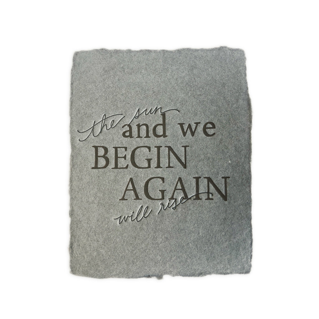 Gray card with torn edges and black text saying, “The Sun Will Rise and We Begin Again”. A matching envelope is included.
