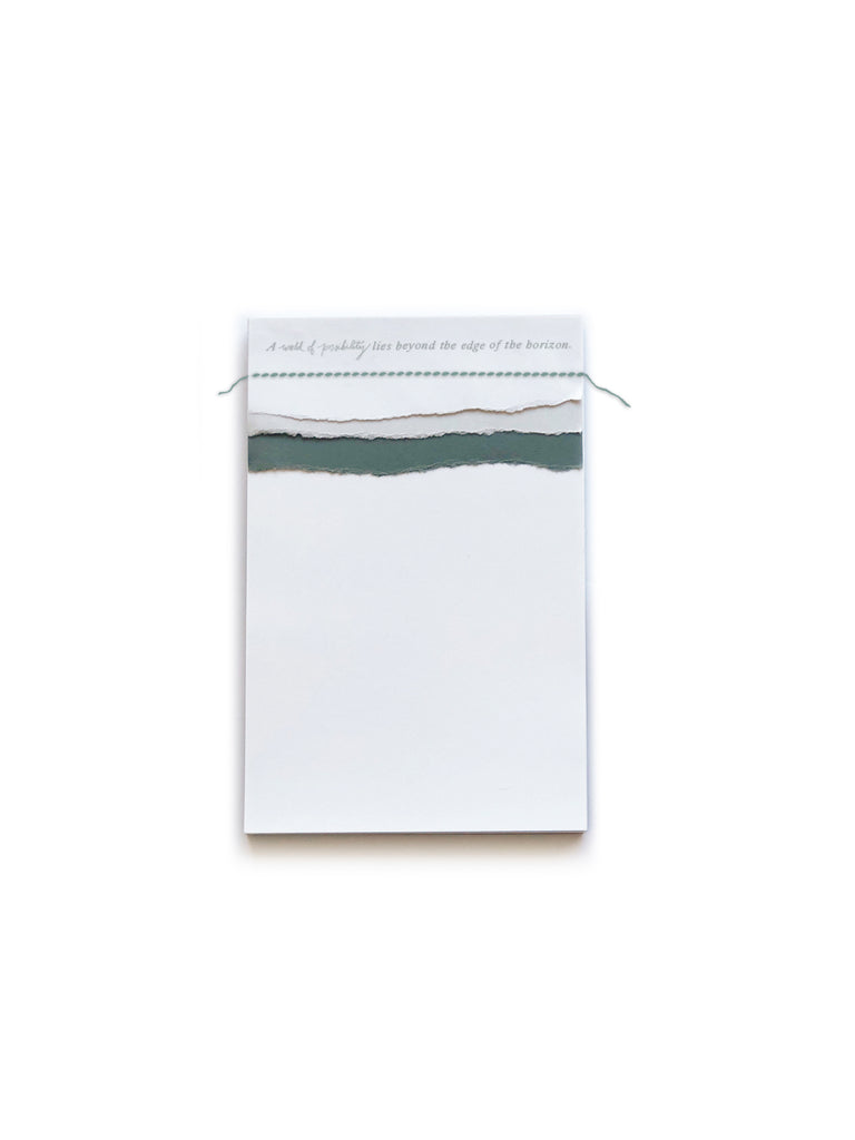 White notepad with gray text saying, “A world of possibility lies beyond the edge of the horizon” across the top.