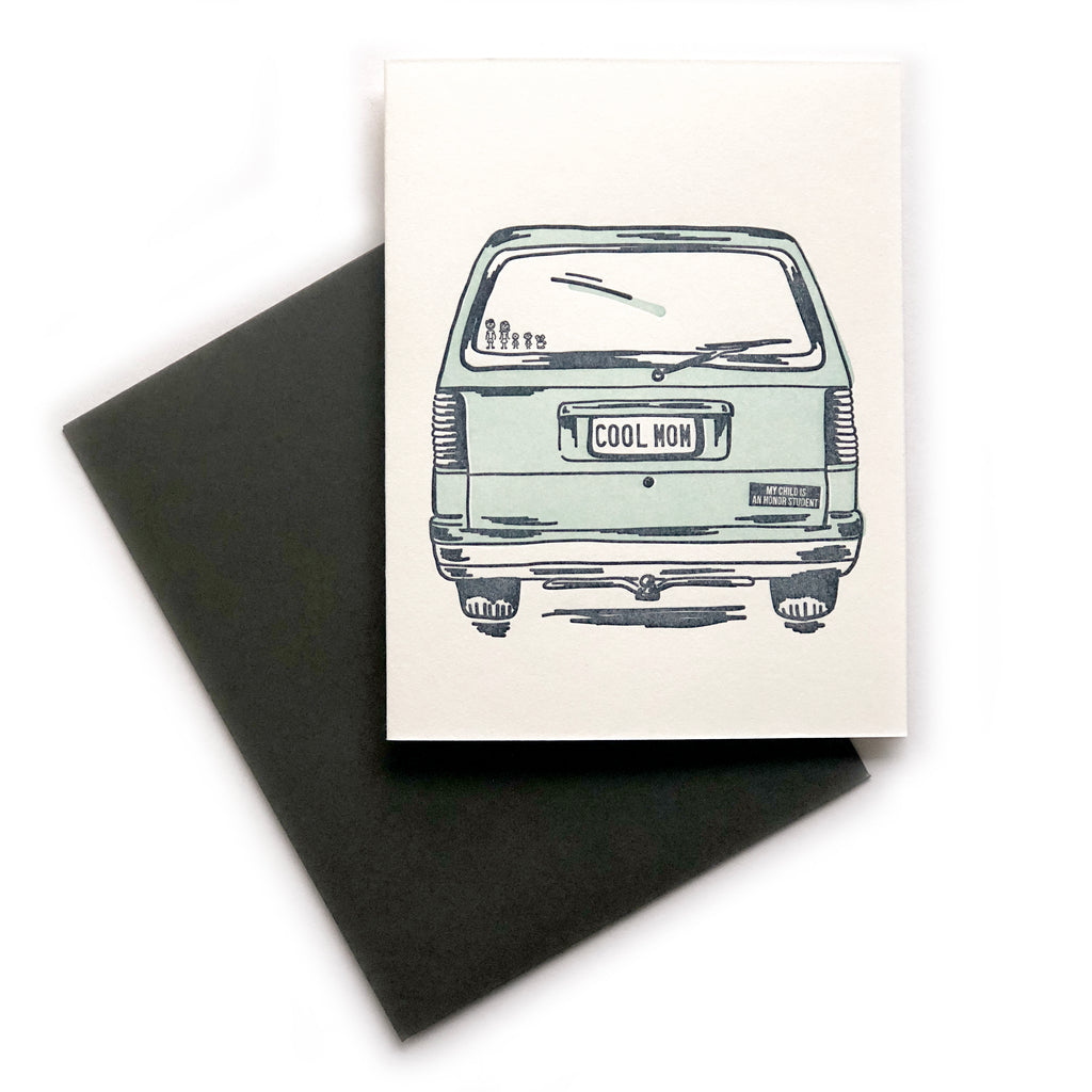 White card with image of the back of a green station wagon car with license plate saying, “COOL MOM”. A black envelope is included.