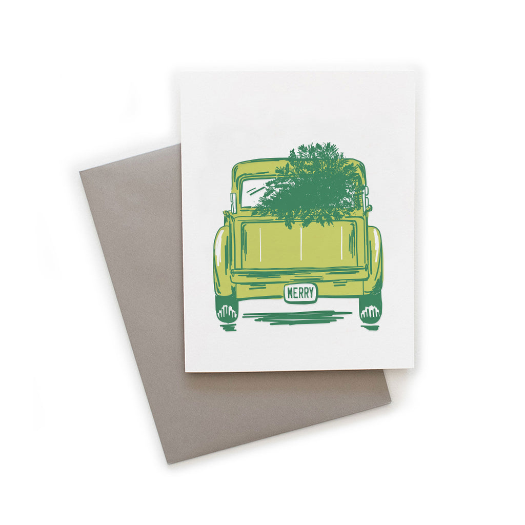 White card with image of a green vintage pick up truck with a green pine tree in the bed. License plate says,
