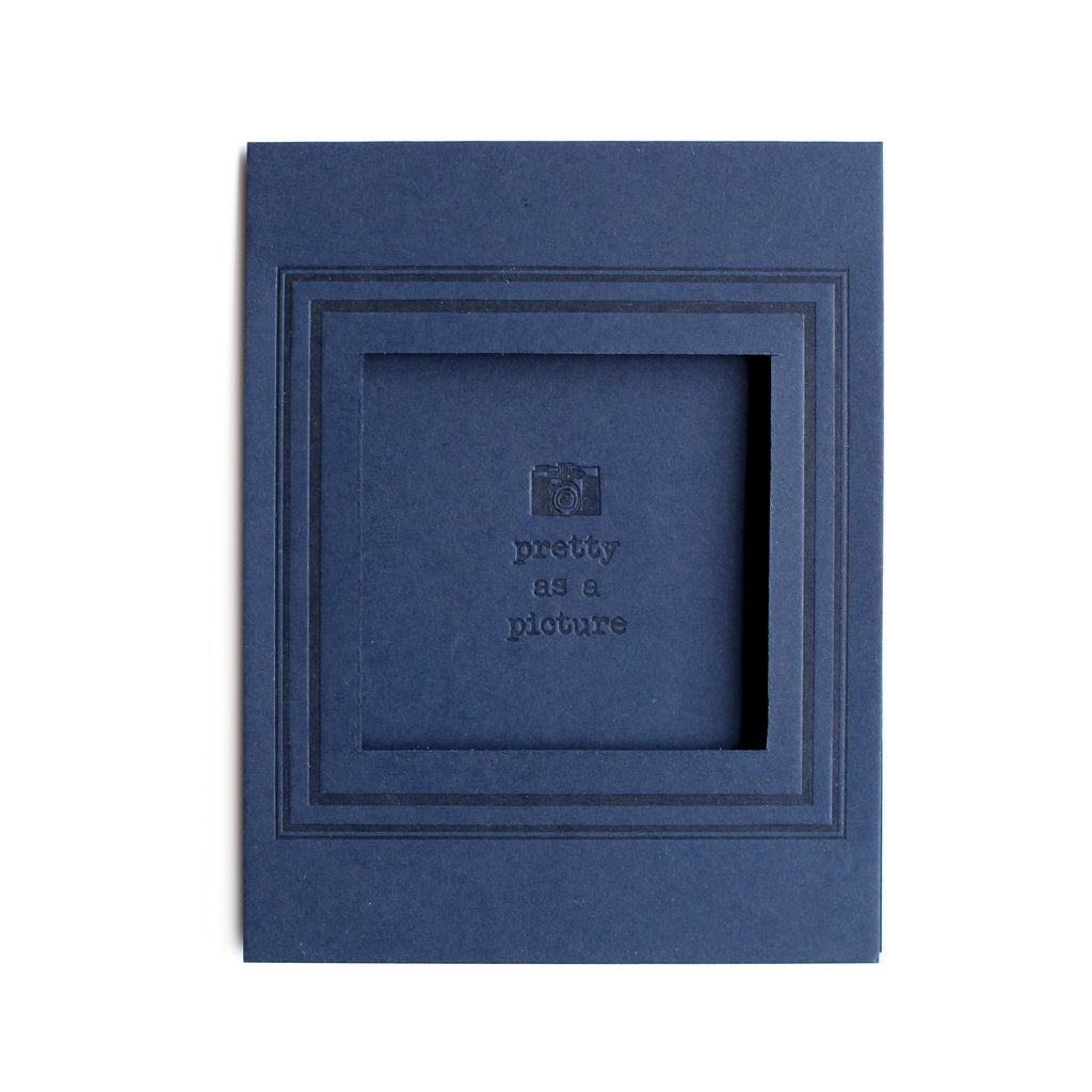 Navy blue card with inset cutout for picture. Background text saying, “Pretty As A Picture” with image of a camera.