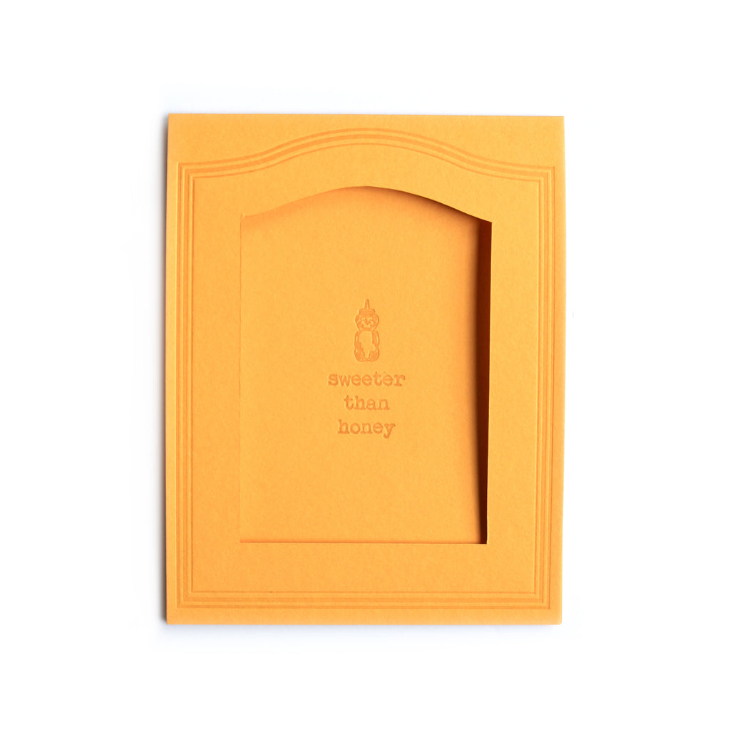 Yellow card with inset cutout for picture. Background text saying, “Sweeter Than Honey” with image of a bottle of honey.