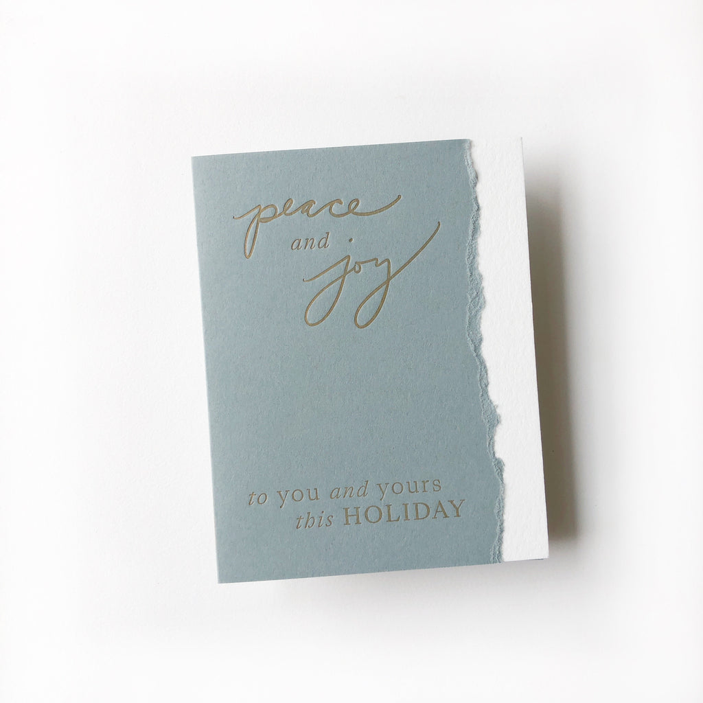 Gray card with white torn edge on right side. Gold text saying, “Peace and Joy to You and Yours This Holiday”. A matching envelope is included.