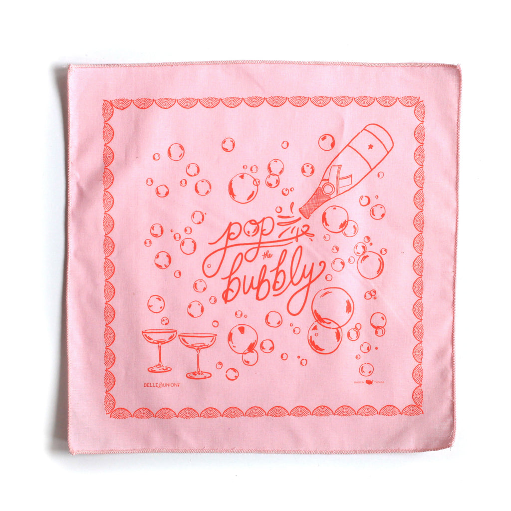 Pink square with red decorative border and red text saying, “Pop the Bubbly”. Images of champagne bottle, bubbles, and two champagne glasses.