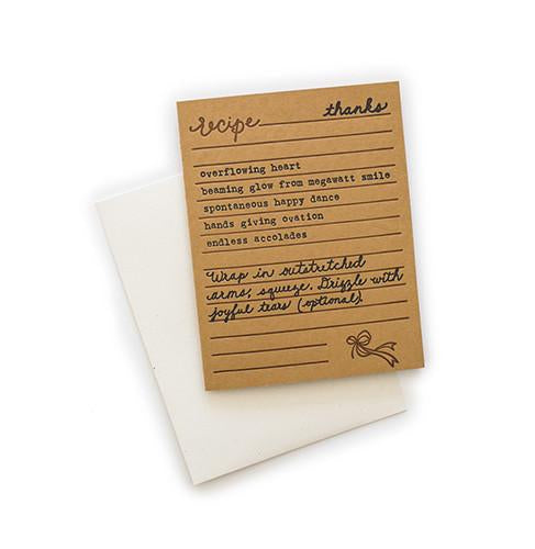 Brown card with black and brown text saying, “Recipe for Thanks: overflowing heart; beaming glow from megawatt smile; spontaneous happy dance; hands giving ovation; endless accolades. Wrap in outstretched arms, squeeze. Drizzle with joyful tears (optional).” Image of a bow ribbon in bottom right corner. A white envelope is included.