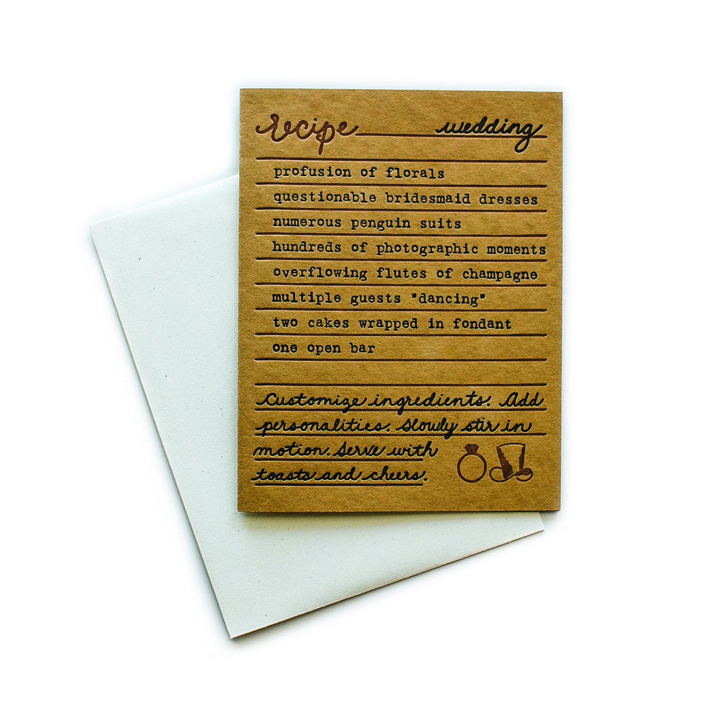Brown card with black and brown text saying, “Recipe for Wedding: profusion of florals; questionable bridesmaid dresses; numerous penguin suits; hundreds of photographic moments; overflowing flutes of champagne; multiple guests dancing; two cakes wrapped in fondant; one open bar. Customize ingredients. Add personalities. Slowly stir in motion. Serve with toasts and cheers.” Image of a top hat and engagement ring in bottom right corner. A white envelope is included.