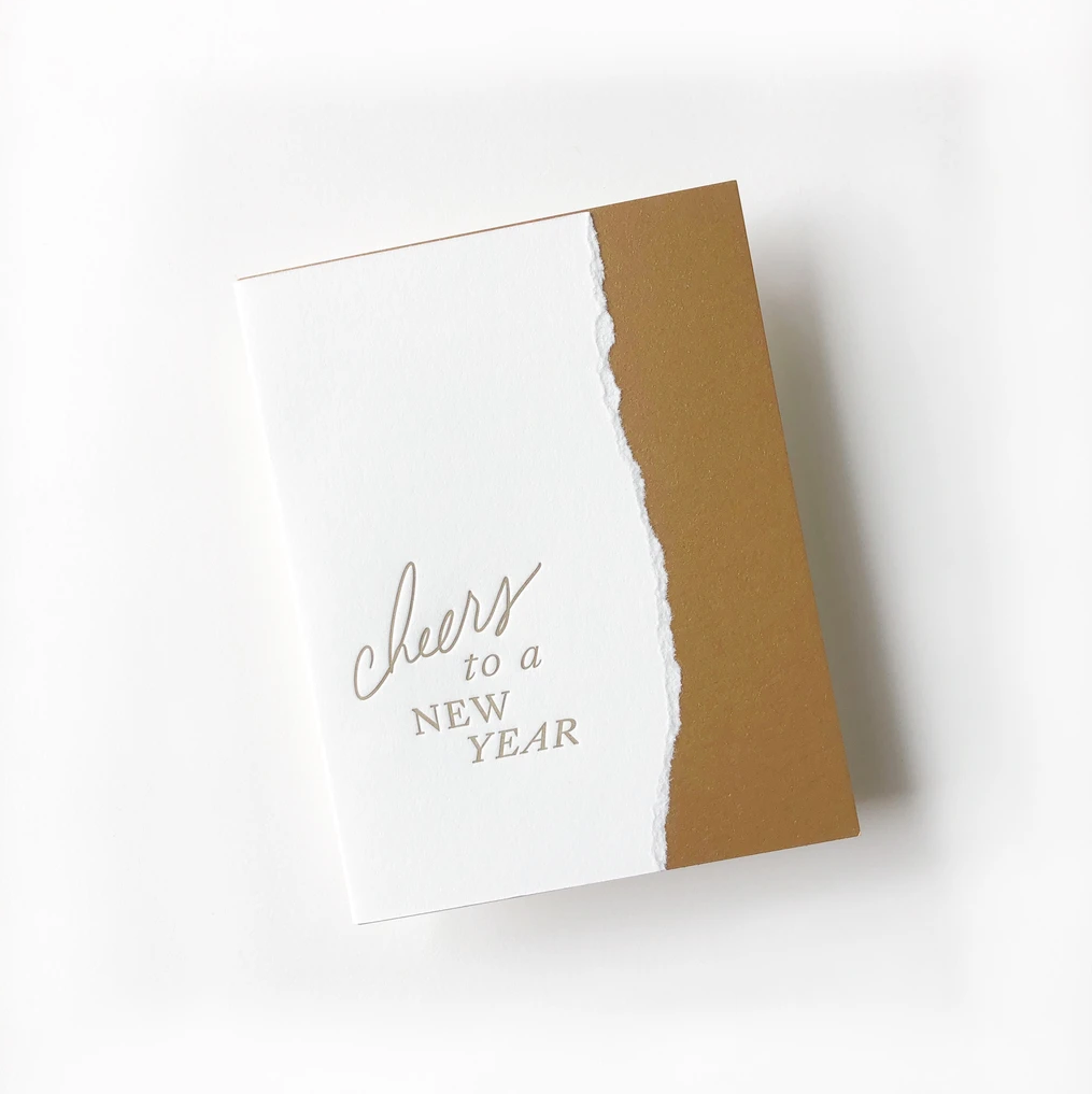 White card with brown torn edge on right side. Brown text saying, “Cheers to a New Year”. A matching envelope is included.