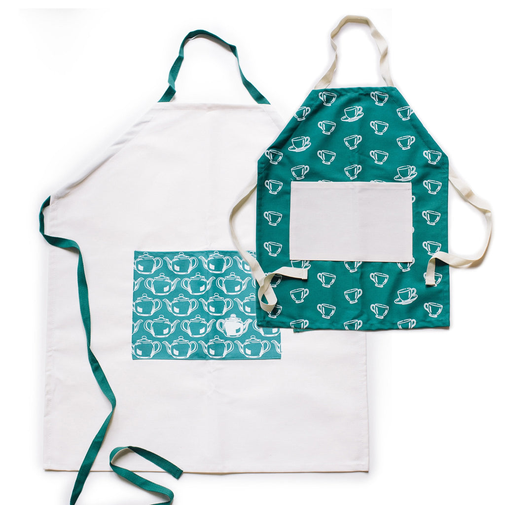 Teal bib apron with white inset square. Images of white teacups. White strap around neck and white strap ties around waist. White bib apron with teal inset square. Image of white teapots. Teal strap around neck and teal strap ties around waist.