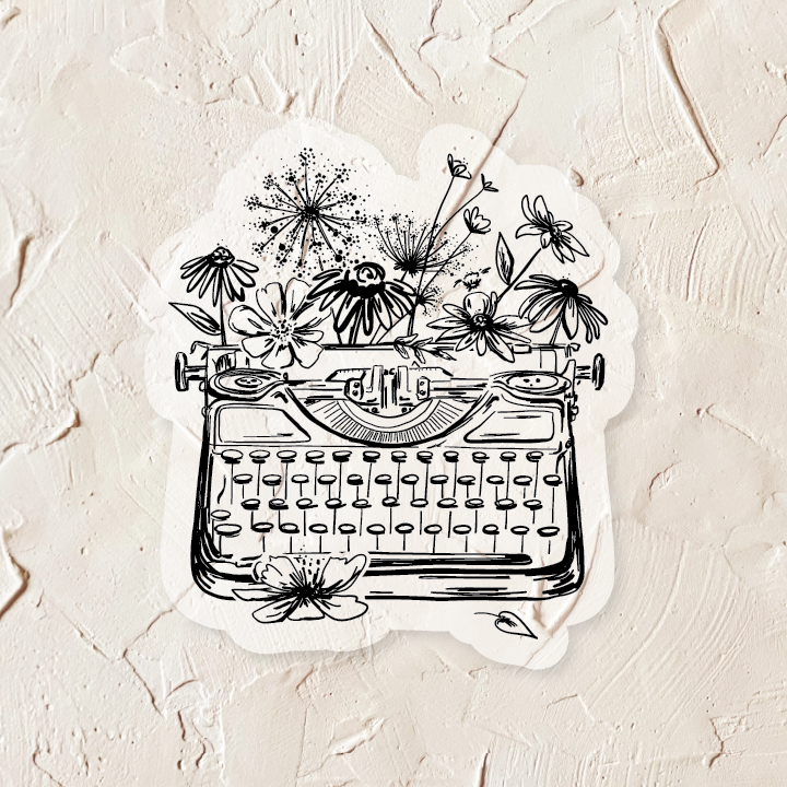 Black and white sticker with image of a vintage typewriter with greenery and flowers.