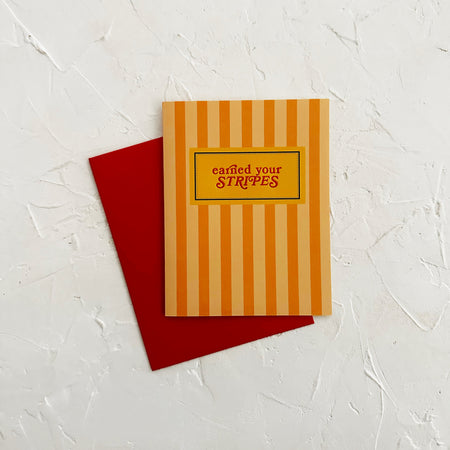 Single greeting card on a textured white surface, with a red envelope and a card with peach stripes and text.